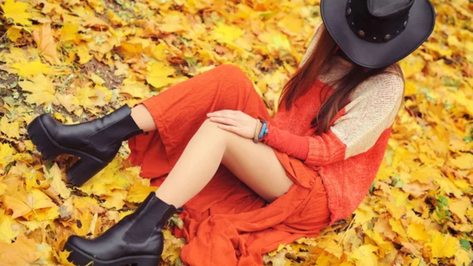 Mulher tirando fotos sobre folhas usando vestido laranja e uma bota preta tratorada
