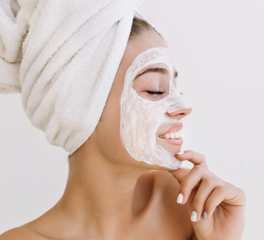 Moça com toalha enrolada na cabeça e creme no rosto.