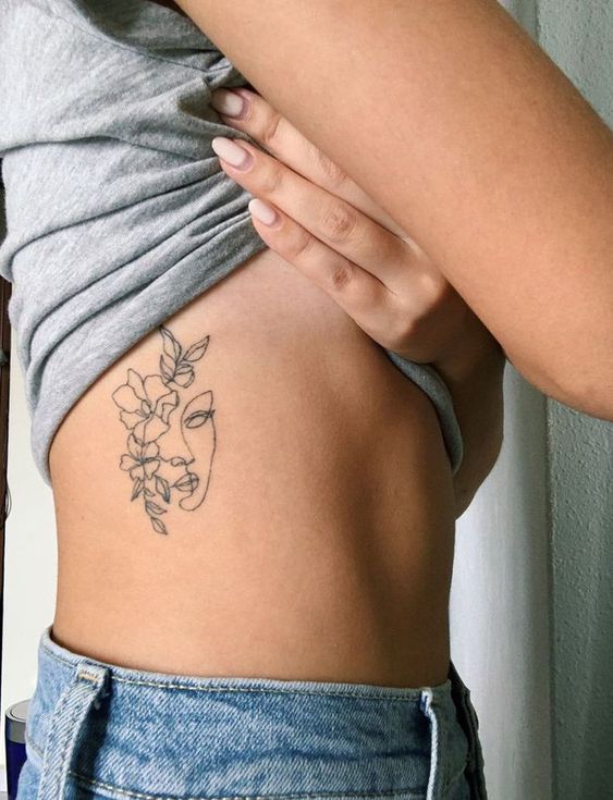 tatuagem de rosto com flores na costela 