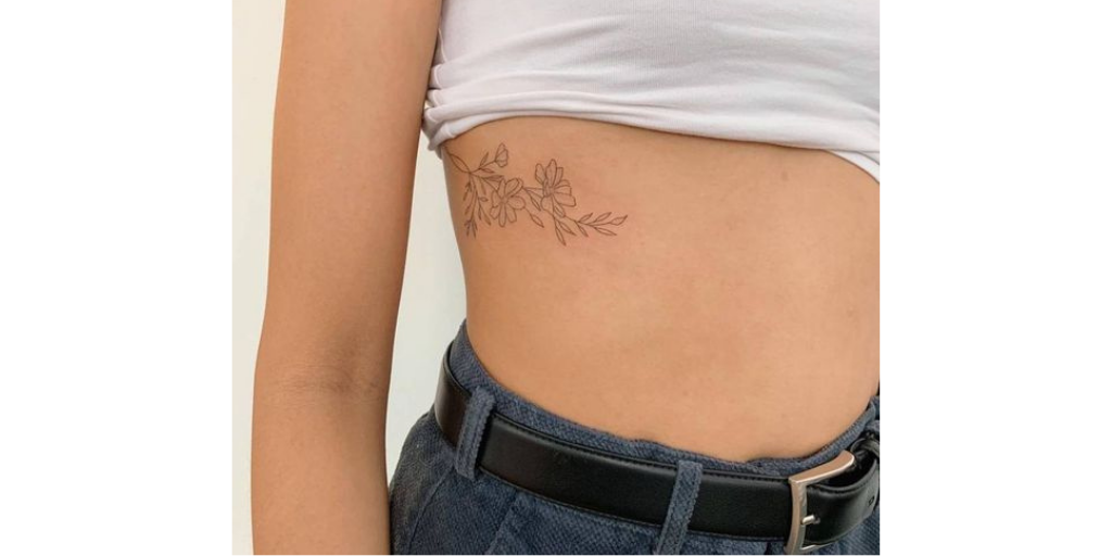 tatuagem feminina de flores com ramo na costela 
