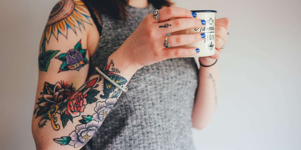 mulher com braço tatuagem segurando xicara 
