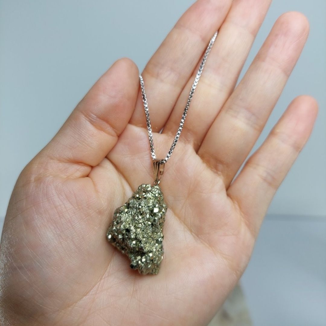 Mão segurando um colar de cristal Pirita