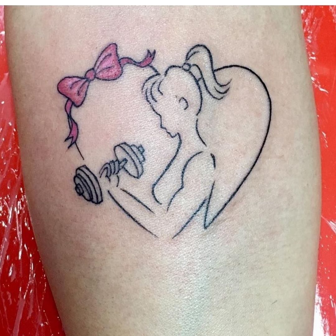 Tatuagem no braço de um coração com uma mulher segurando um peso de academia.