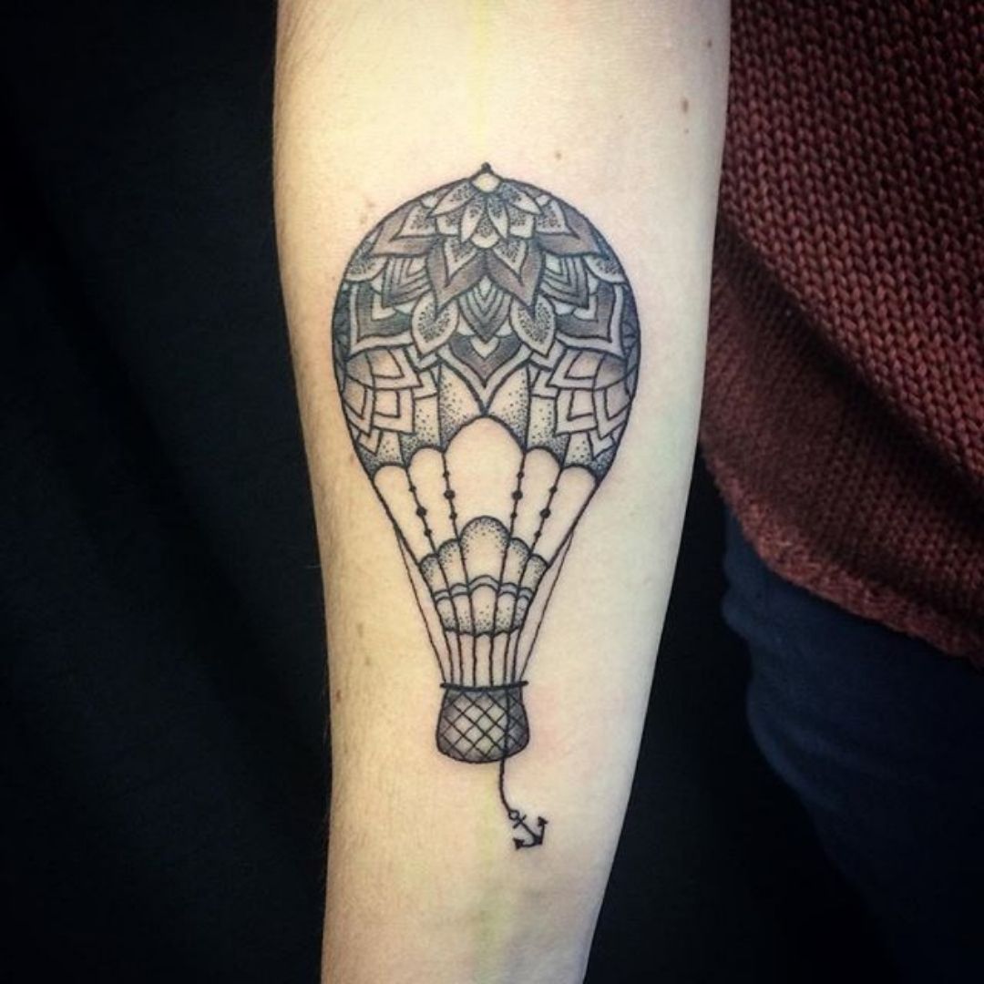 Tatuagem feminina de um balão carregando uma ancora  no braço.