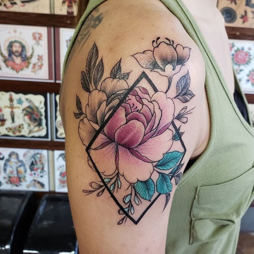 Tatuagem no braço com uma flor colorida parcialmente dentro de um triangulo o com desenho assimétrico 