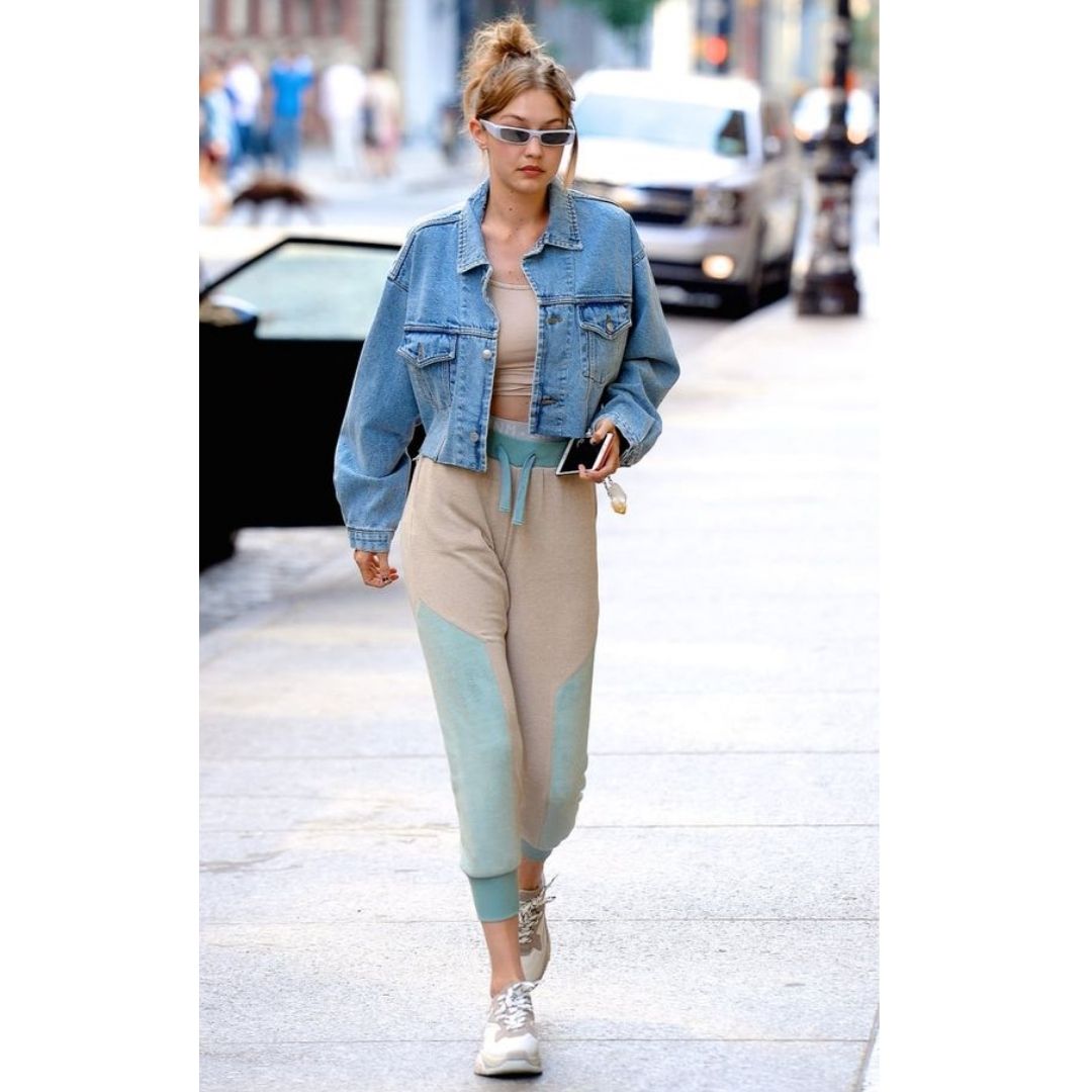 Mulher andando na rua com um moletom azul e nude jaqueta jeans e tênis 