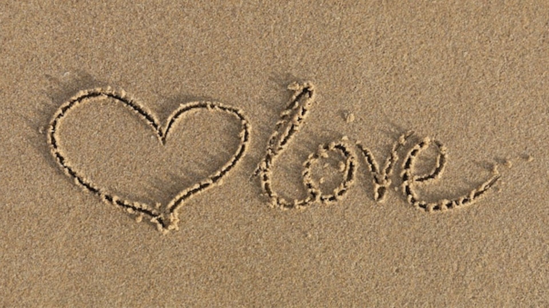 Coração e a palavre love desenhado na areia representando o amor 