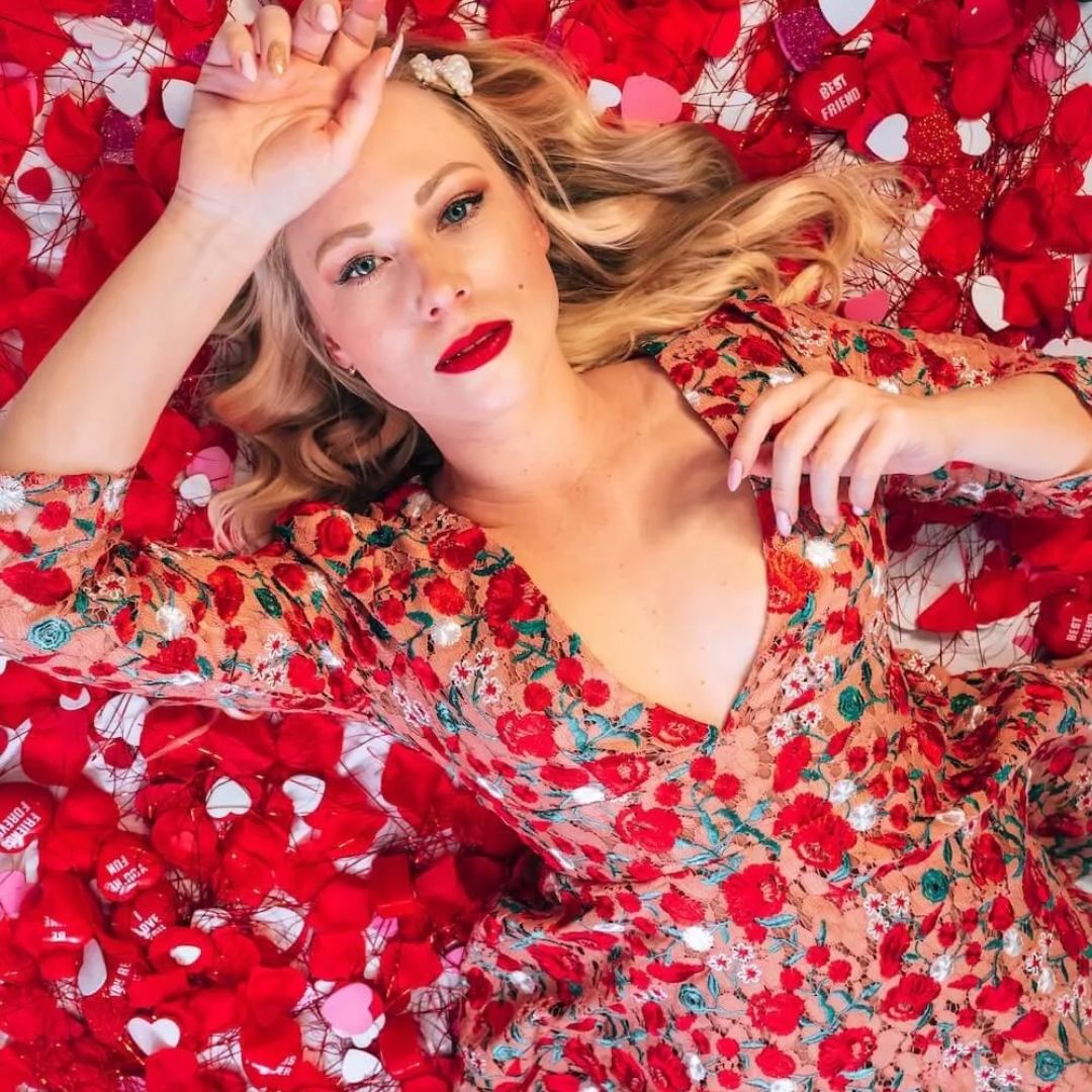 Mulher de vermelho deitada sobre varias pétalas de rosas vermelhas
