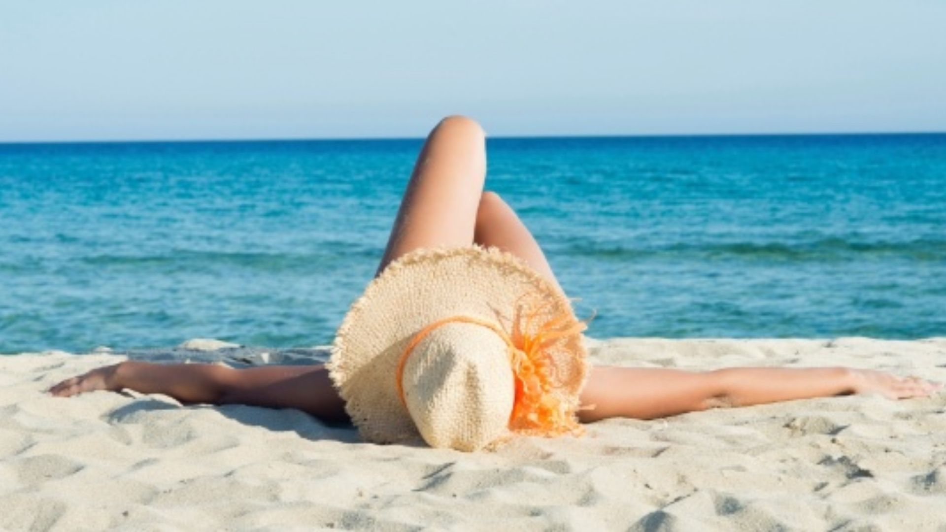 Mulher ditada na areia mostrando apenas o chapéu