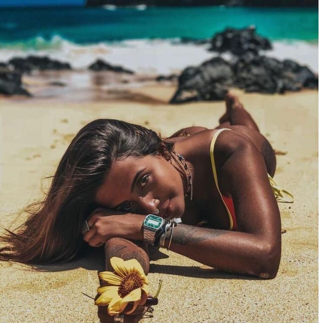 Mulher deitada na areia olhando para câmera com um girassol na mão