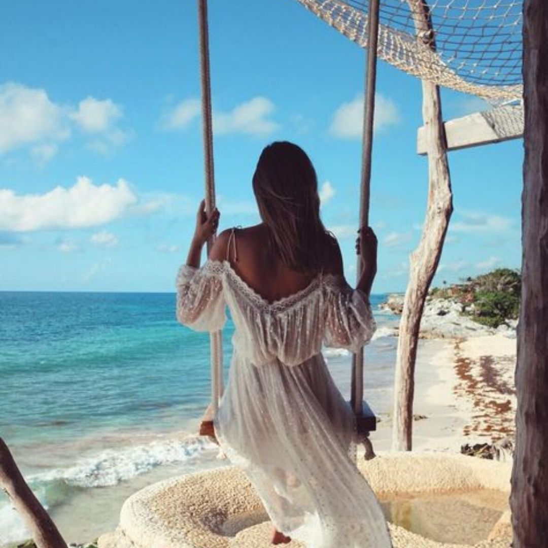 Mulher vestido de branco em um balanço de frente para a praia