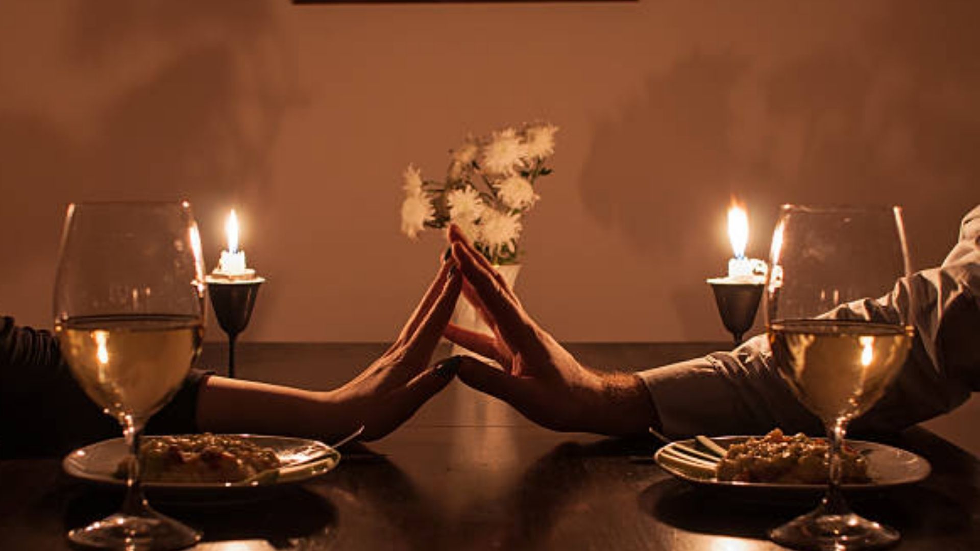 Foto de duas mãos se encontrado sobre uma mesa a luz de velas