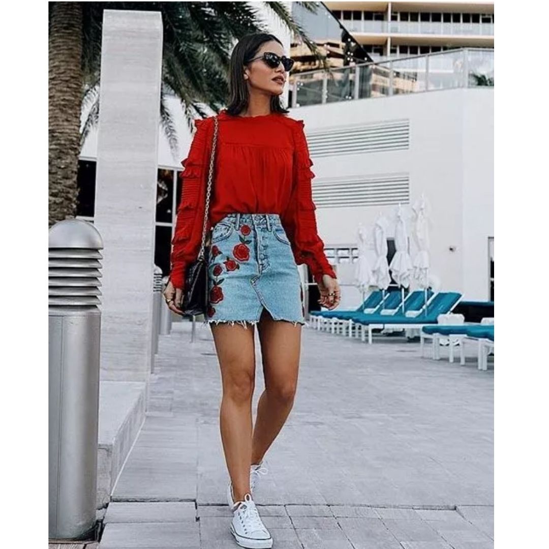 Mulher na rua com uma blusa vermelha , saia jean e tênis branco