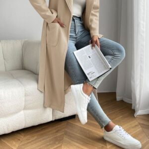 Pernas de uma mulher usando um look de inverno com tênis branco enquanto lê uma revista