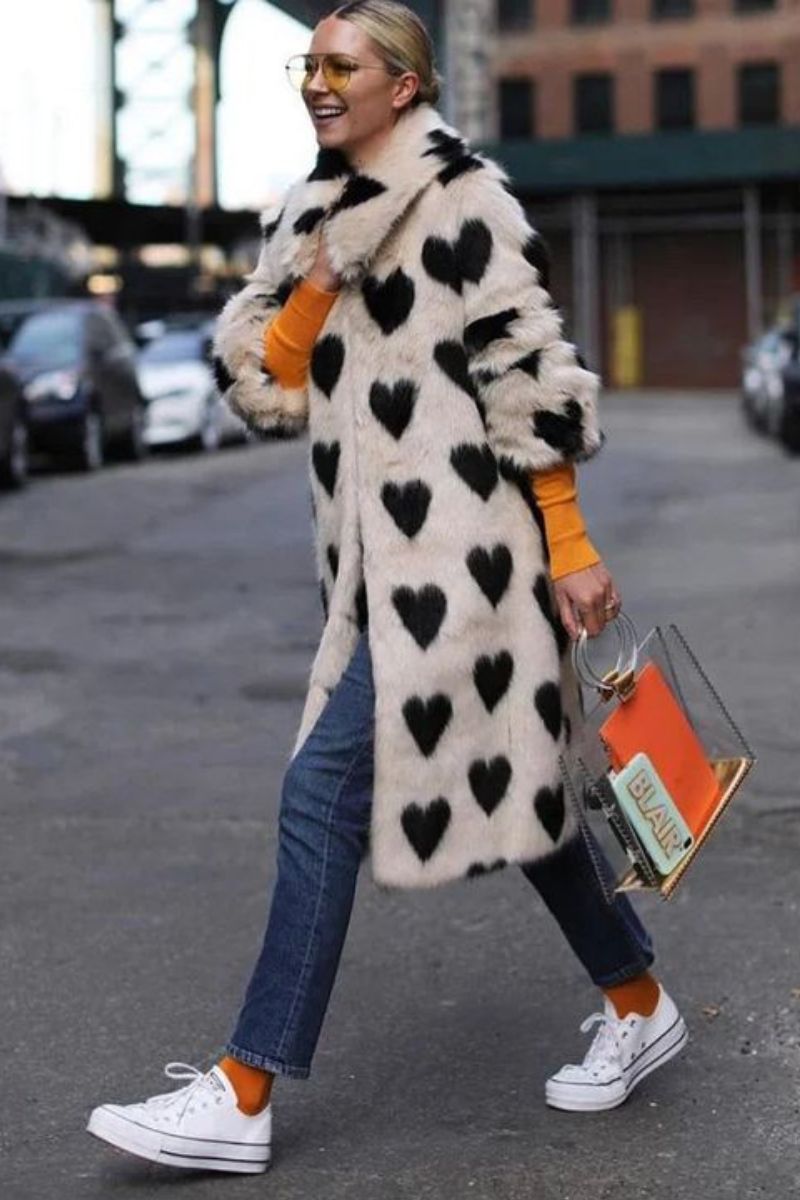 Mulher loira caminhando demonstrando como usar um look de inverno com tênis com um sobretudo furry de corações
