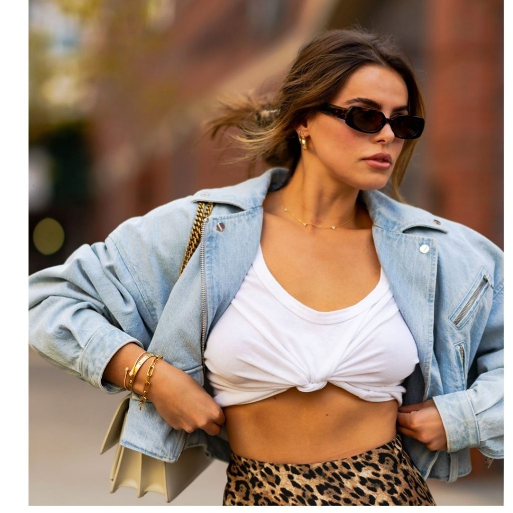 Modelo andando  na rua com um look na composto por uma camisa e um uma blusa amarrada, na moda saia do básico