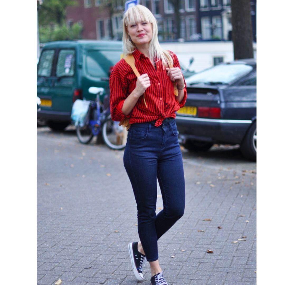 Modelo andando  na rua com um look na composto por uma calça jeans e camisa vermelha básica na moda saia do básico