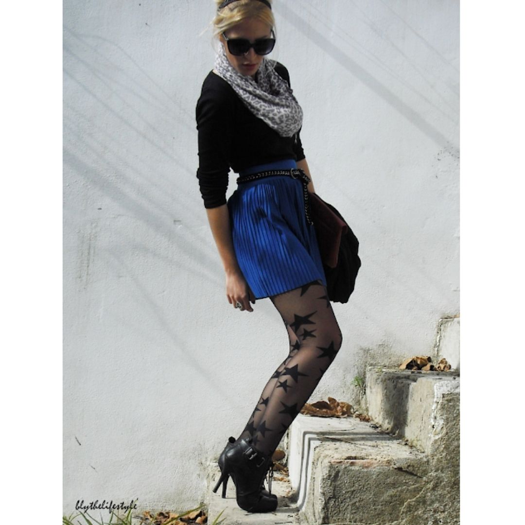 Mulher subindo uma escada com uma saia azul blusa preta, meia-calça arrastão e botas