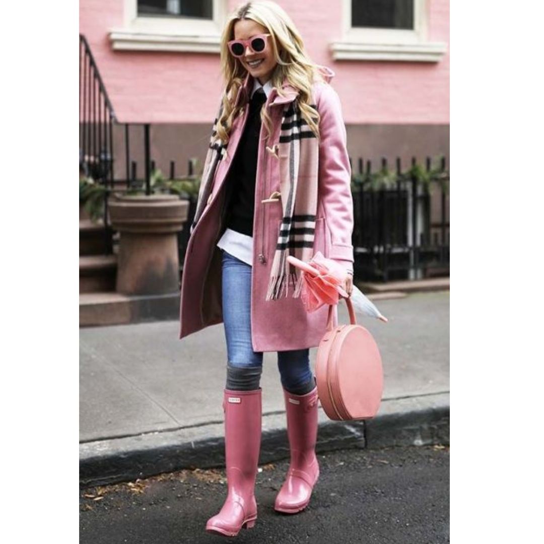 Mulher usando look com botas coloridas e rosa, um sobretudo rosa um lenço xadrez, calça jeans