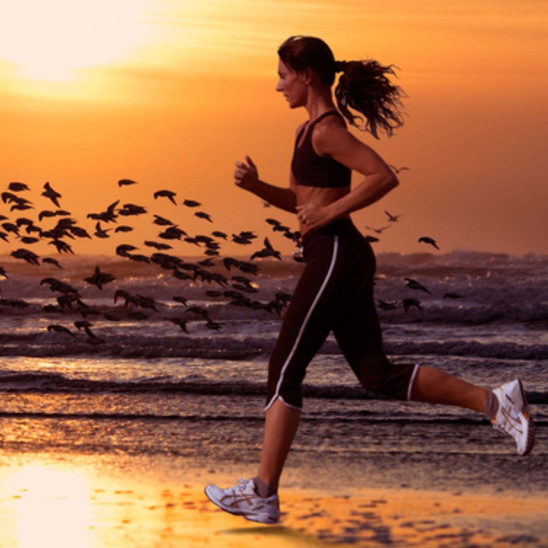 Mulher correndo na praia durante pôr do sol 
