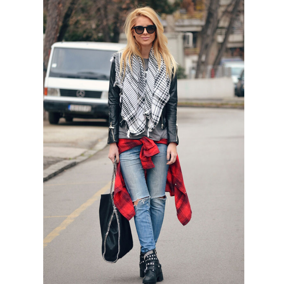 Mulher na rua pousando para fotos, reta, calça jeans, jaqueta preta e um lenço xadrez