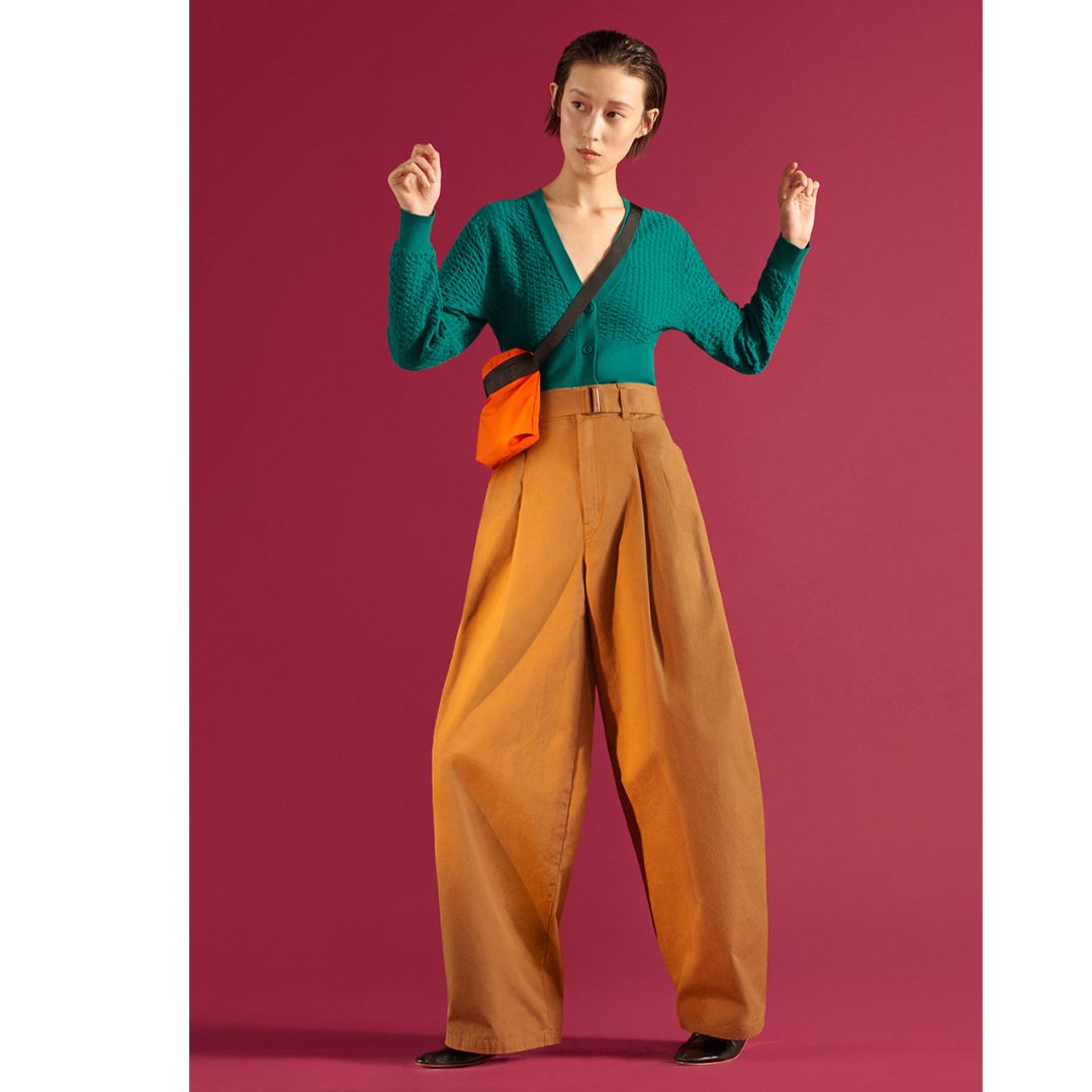 Modelo posando para foto com cardigan verde e calça alfaiataria na cor laranja 