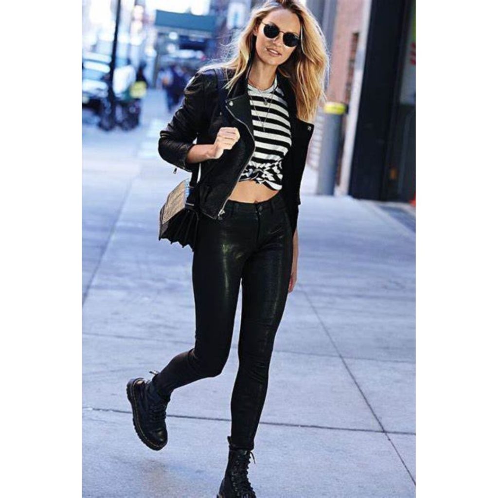 Mulher andando na rua usando uma blusa listrada uma jaqueta preta , calça de couro e coturno 