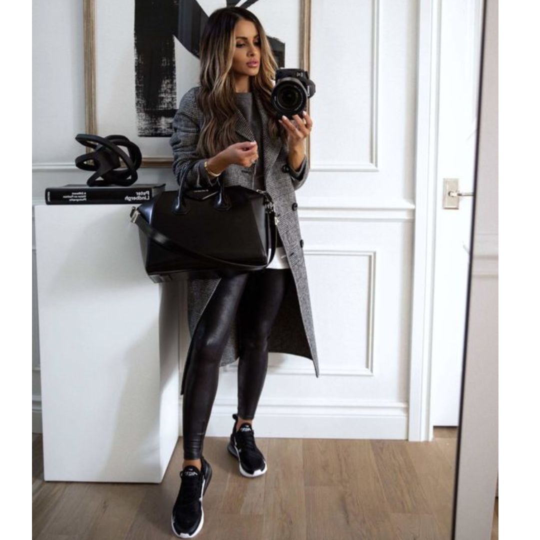 Mulher tirando foto no espelho, usando um look preto composto por calça de couro e tênis preto 