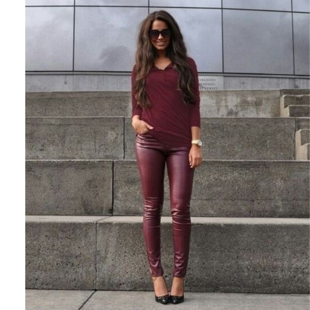 Mulher posando para fotos de frente a uma escada usando uma blusa e uma calça de couro na cor  vinho 