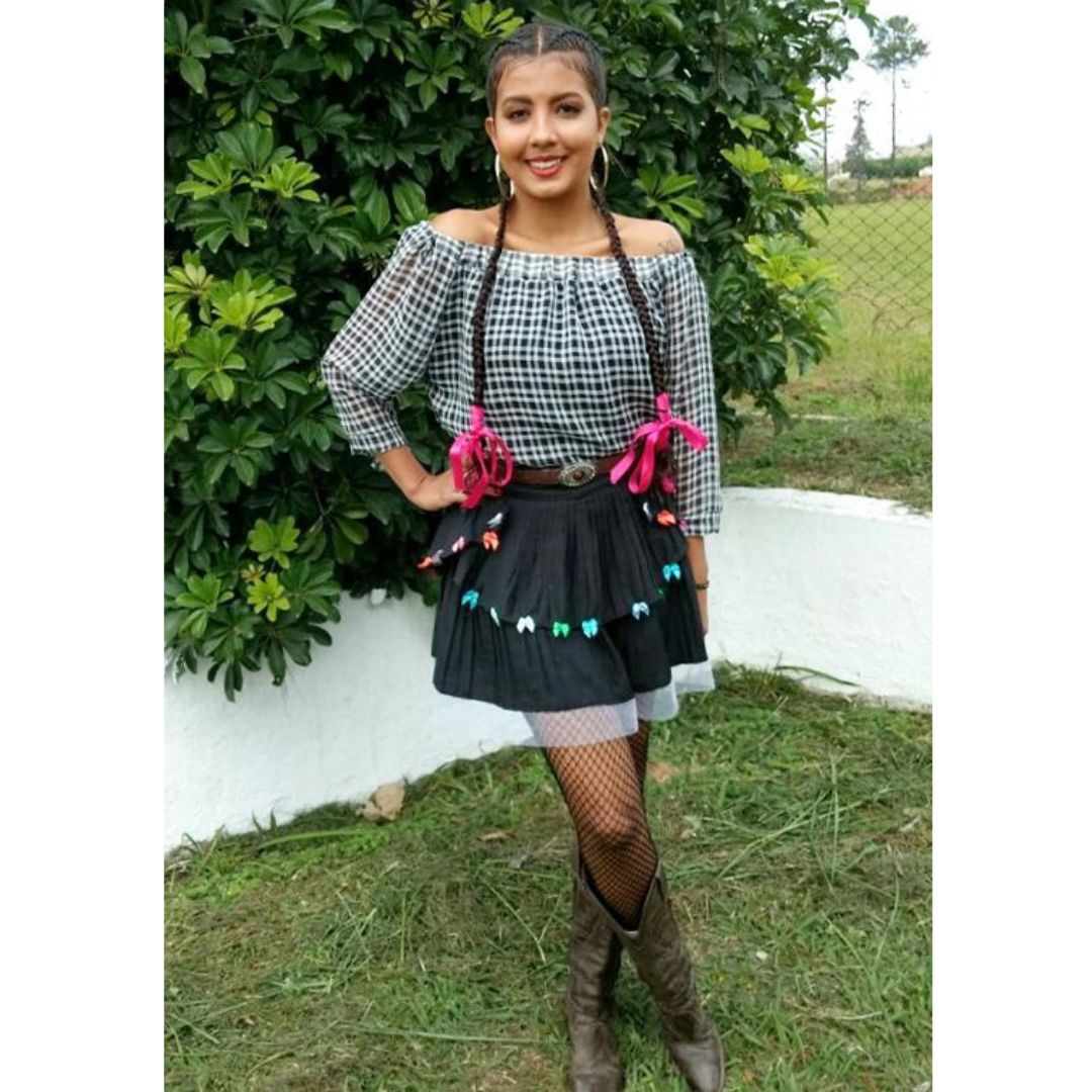Mulher tirando fotos com uma saia e uma blusa xadrez customizado de bandeirinhas para o look de festa junina