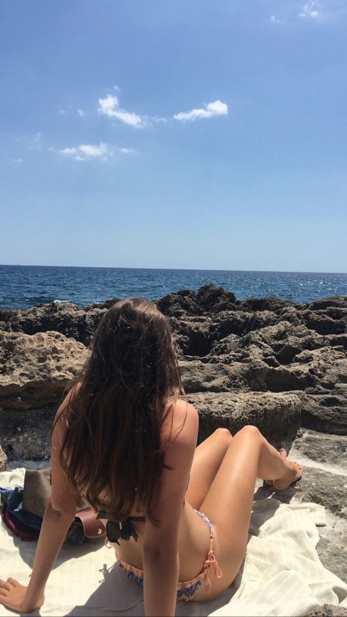 menina sentada na praia olhando o mar