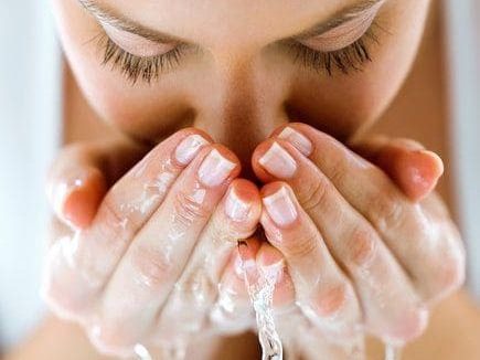 Mulher lavando o rosto em rotina de skincare noturna