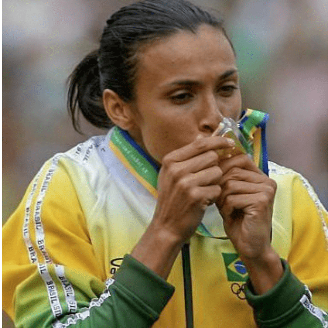 Marta - melhor jogadora de futebol feminino beijando uma medalha, usando uniforme da seleção brasileira