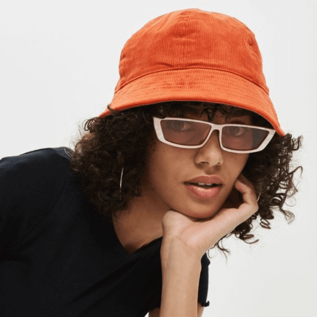 Menina usando camiseta preta, óculos com armação branca e bucket hat laranja