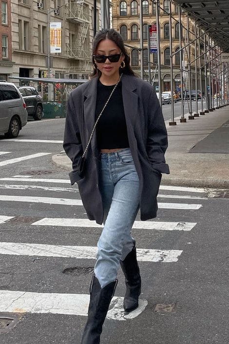 Mulher usando look com bota western preta com calça jeans e blazer cinza