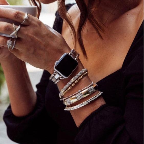 Mulher segurando caneca com um braço cheio de pulseiras de prata e relógio