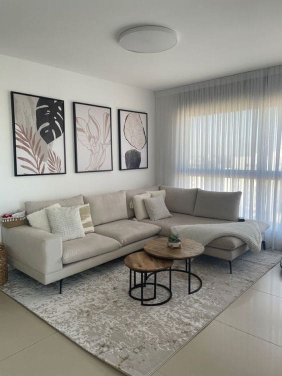 Sala estilo minimalista com sofá claro, com almofadas, um tapete branco e cinza e uma mesinha de centro em madeira e pernas de ferro preto