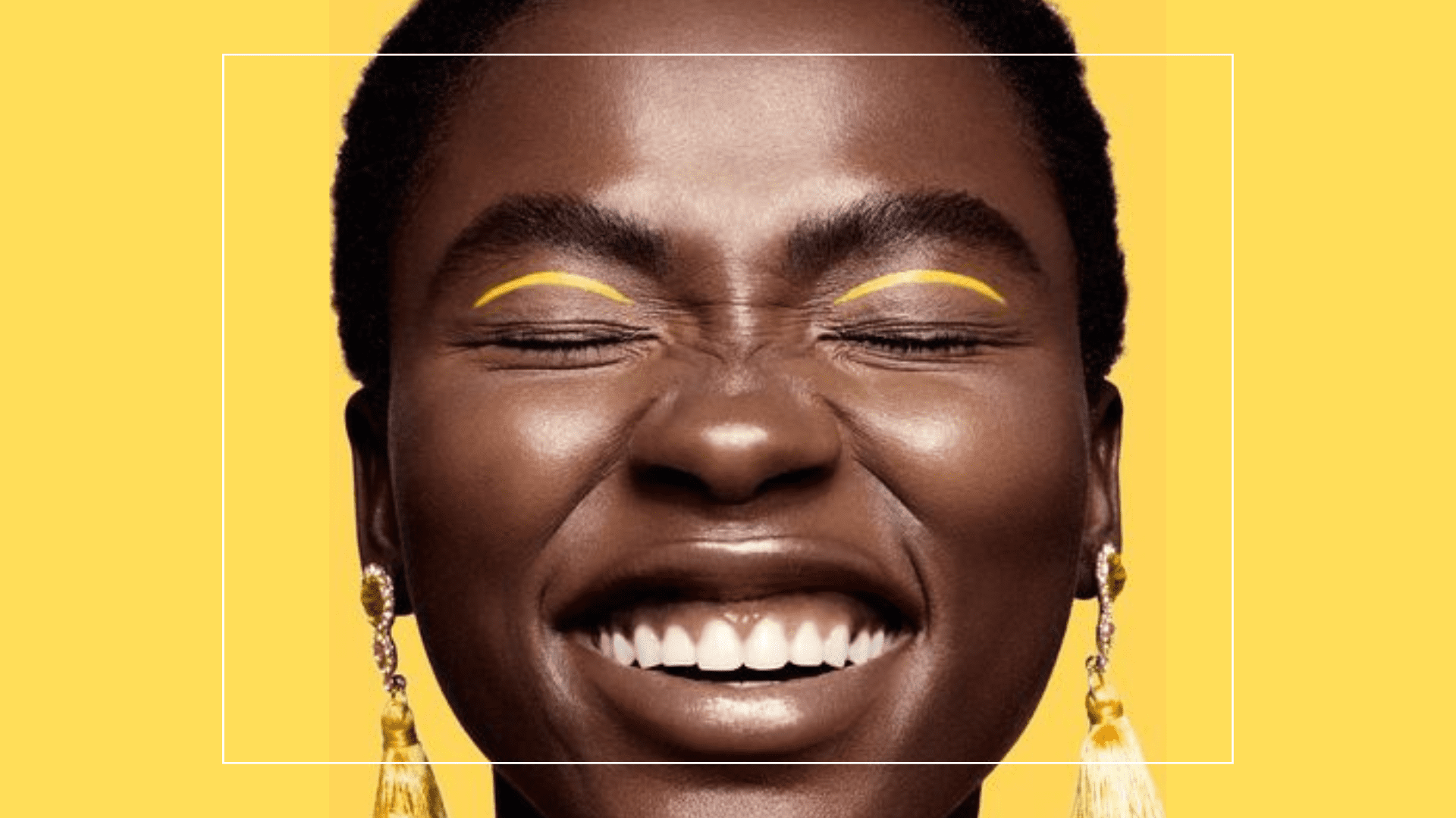 Mulher negra sorrindo usando uma maquiagem como delineado colorido amarelo