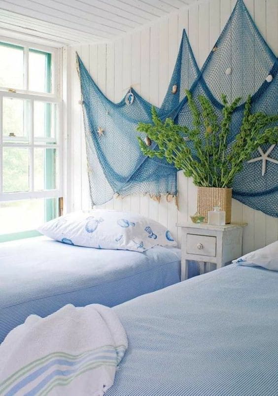 Quarto com duas camas com lençóis azuis e rede com conchas e estrelas na parede
