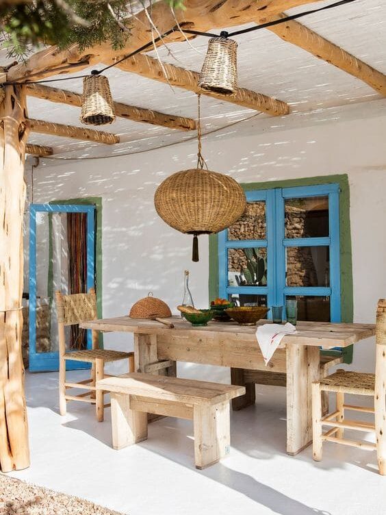 Quintal com elementos que remetem a praia, com mesa e bancos de madeira e cores azuis na porta e janela