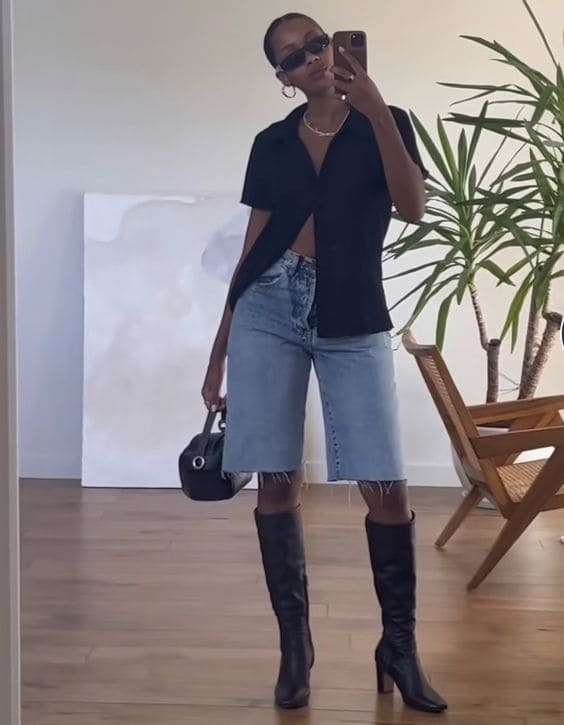 Mulher tirando foto para mostrar o look com bermuda jeans e bota