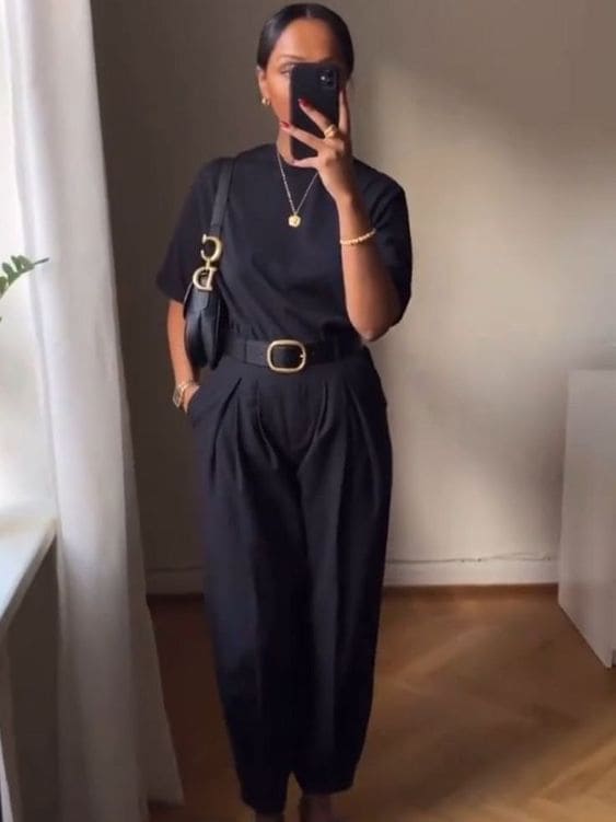 Mulher usando look com camiseta preta, calça de alfaiataria, bolsa e cinto que combinam com sandália para o verão