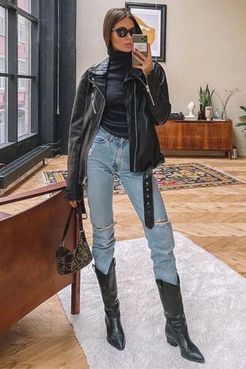 Mulher usando uma roupa que combina com bota composta por uma jaqueta de couro jeans sobre uma camiseta preta, jeans de lavagem clara e botas de cano médio
