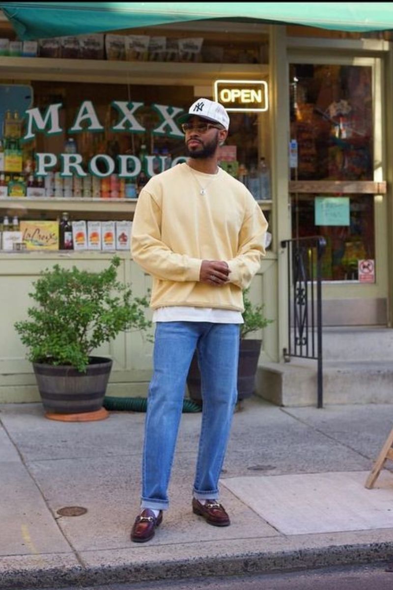 Homem usando um look de inverno masculino composto por um suéter amarelo, jeans e mocassim de couro