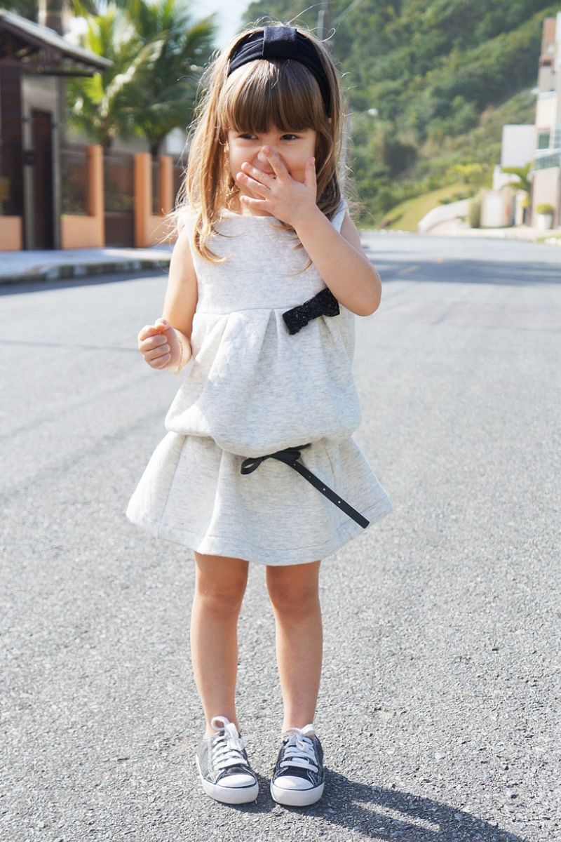 Menina pequena usando um look infantil com All Star de cor preta e vestido de cor clara
