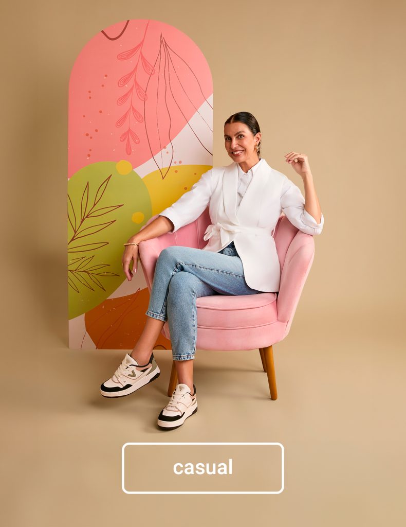 Mulher com visual casual, usando jeans, blazer branco e tênis, sentada em poltrona rosa — inspiração moderna e confortável de presente de Dia das Mães.