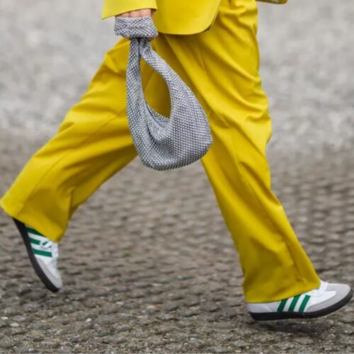 Pernas de uma mulher com roupa predominantemente amarela exibindo como usar calça pantalona com tênis Adidas