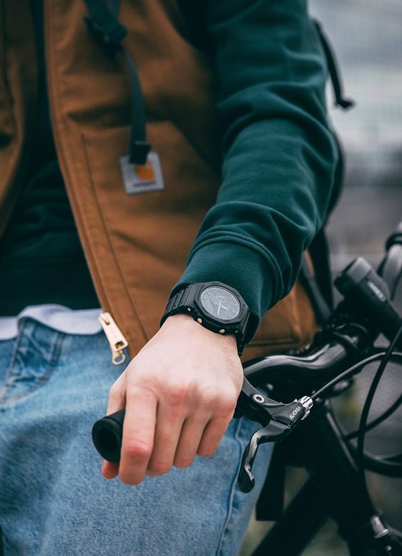 Homem recostado sobre uma bicicleta exibindo seu relógio preto que é uma boa ideia de presente dia dos namorados para homens
