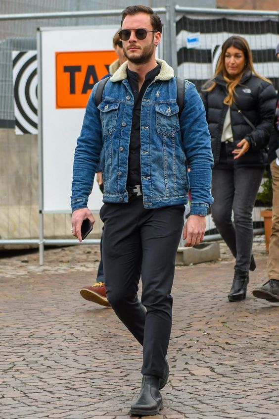 Homem usando óculos escuros redondos e um look com jaqueta jeans masculina com bota