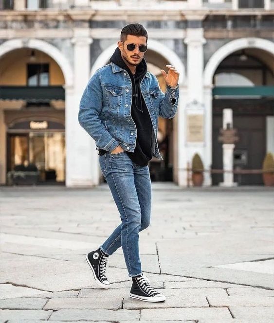 Homem usando um look com jaqueta jeans masculina sobreposta a um moletom preto